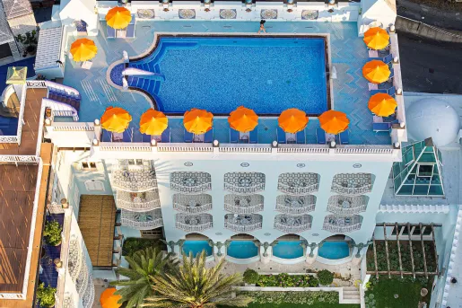 Aerial view of the rooftop pool and sun deck with bright orange umbrellas at the Palazzo Manzi Terme & Spa in Casamicciola Terme on the island of Ischia, Italy.