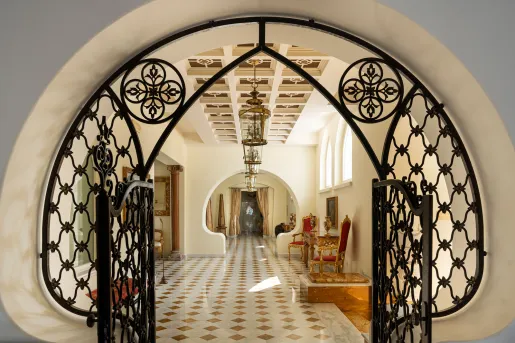 The elegant entryway featuring an arched wrought-iron gate framing a long, bright hallway with a patterned tile floor and classic hanging lanterns at the Palazzo Manzi Terme & Spa in Casamicciola Terme on the island of Ischia, Italy.