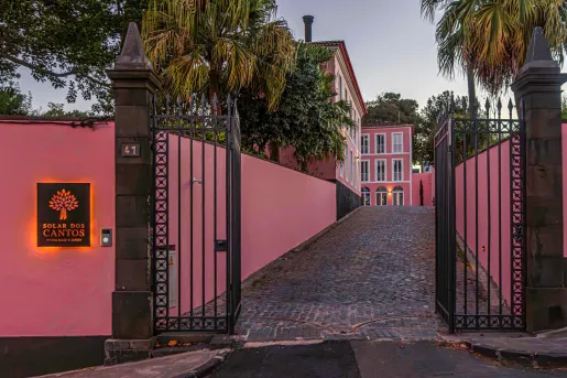 Exterior view of a hotel driveway with pink walls and a black gate