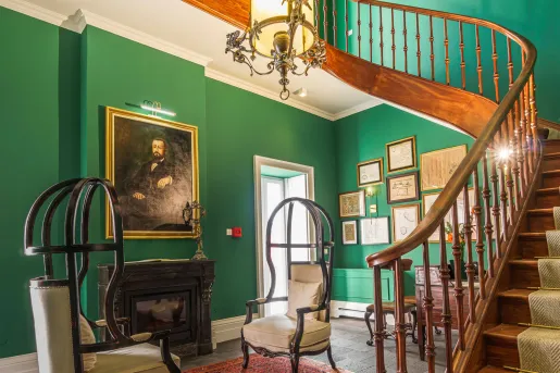 Room with green walls with a wooden staircase and portraits on the walls