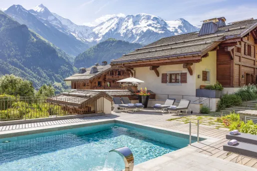 Beige building with an outdoor pool in front, with tall mountains in the distance