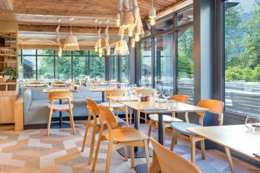 Restaurant dining room with wooden chairs and tables, with tall windows