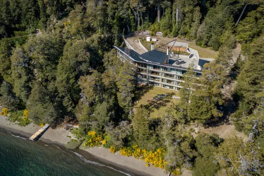 Aerial view shows the lakeside  multi-level Calfuco Wine Hotel & Spa surrounded by forest in Neuquén, Argentina.