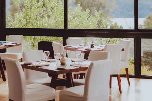 Modern dining room with wood tables and white-covered chairs at Hotel Alto Traful. 