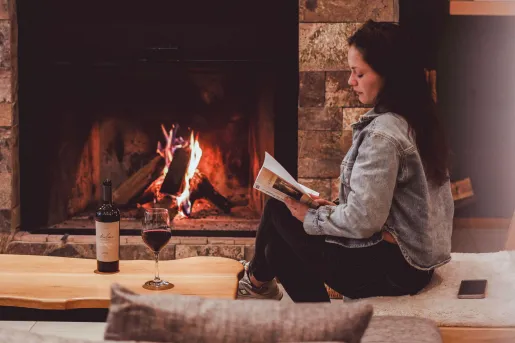 A woman reading near a wood burning fireplace while having a glass of red wine at Hotel Alto Traful. 