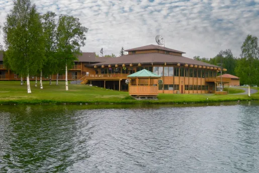 Large cabin-styled building in front of a lake with a grass field