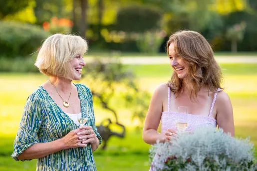 Two women looking at each other, smiling with a grass field in the background