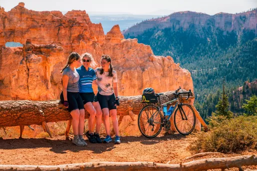 Three women leaning on a log, with their arms around each other while they smile