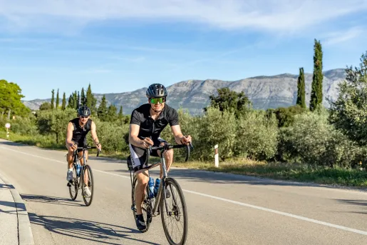 Two people biking on a road, with a large valley and trees in the background