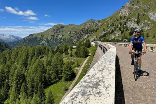 Man biking on a road, looking over a ledge towards a valley