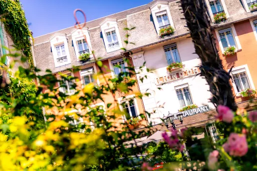 Exterior view of white and brown hotel building with plants and bushes in front