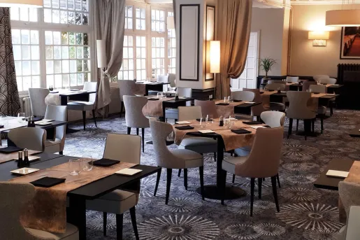 Restaurant dining area with black tables and beige, cushioned chairs, with brown table cloths on each table