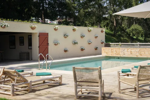Outdoor pool surrounded by woven chairs and a building with potted plants hanging