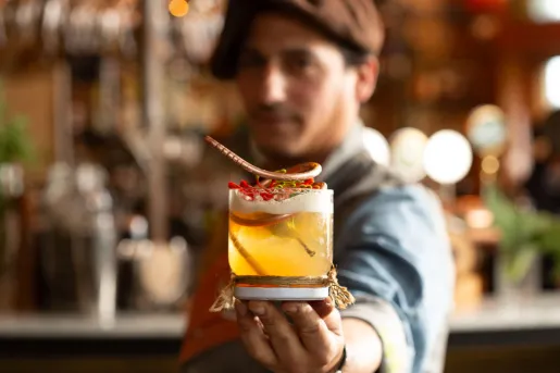 Man holding up a cocktail with a bar in the background