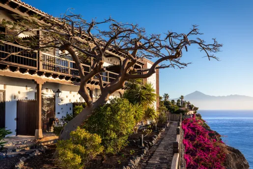Exterior view of two-story building with a tree in front, and a cliff with the ocean down below