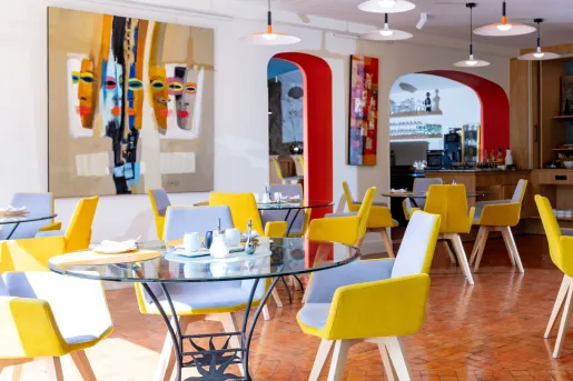 Indoor dining area with glass, circular tables with yellow chairs surrounding