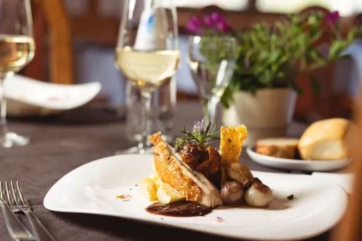 Dining table with a white plate with food an a wine glass in the background