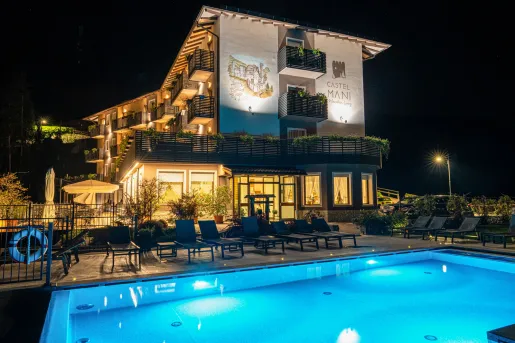 Exterior, evening view of a hotel building with an illuminated pool in front