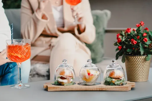 Woman holding a glass, with three little trays of food on the table
