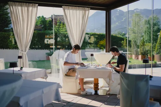 Two men sitting at a white dining table at a restaurant, with large windows along the walls