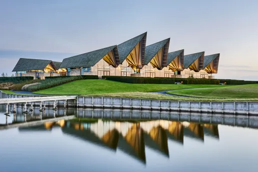 Exterior view of large hotel building with a grass lawn and lake in front