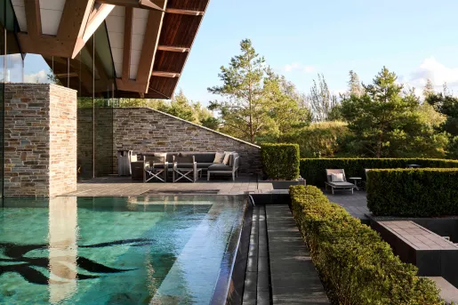 Outdoor pool with trimmed bushes in front and tall trees in the distance
