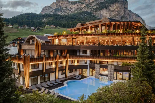 Exterior view of large hotel building with illuminated rooms and an outdoor pool