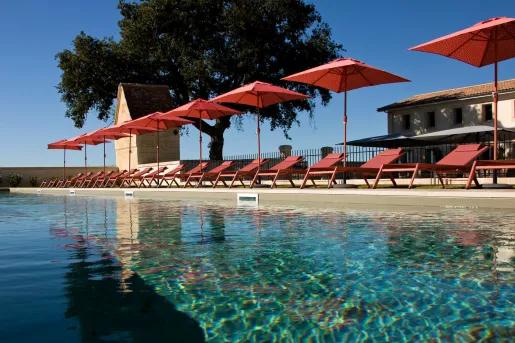 Outdoor pool with a row of red reclining chairs and umbrellas
