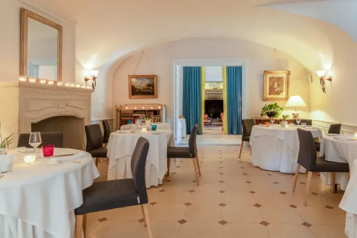 The dining room at Manoir d'Hautegente features arched ceilings, terracotta tiled floors, and dark upholstered chairs with a stone fireplace.