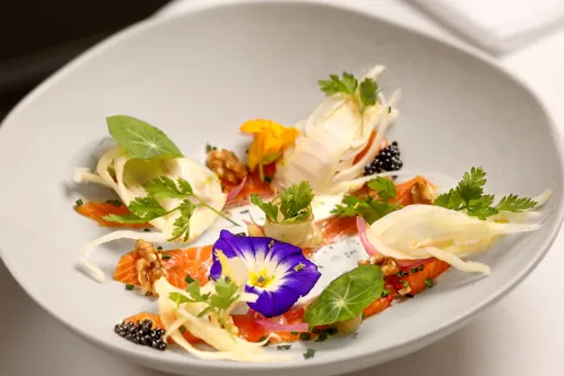 A fine-dining dish features cured salmon served with fennel, edible flowers, walnuts, and caviar.
