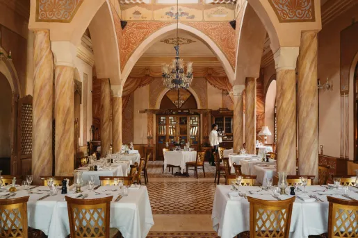 Le Great Room dining room inside the Al Moudira Hotel in Luxor, Egypt features an ornate, palace-like setting featuring hand-painted ceilings and towering marble pillars.