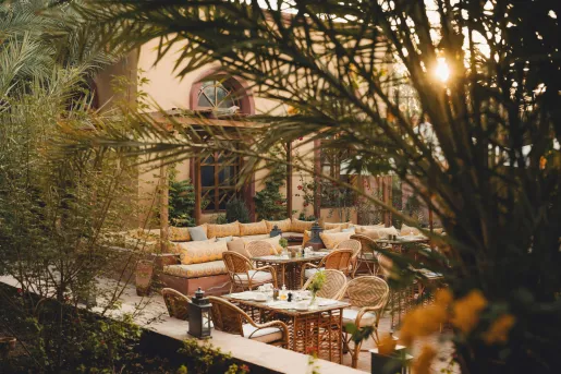 The outdoor courtyard patio restaurant at the Al Moudira Hotel in Luxor, Egypt that features an open-air dining space framed by lush gardens and palm trees.