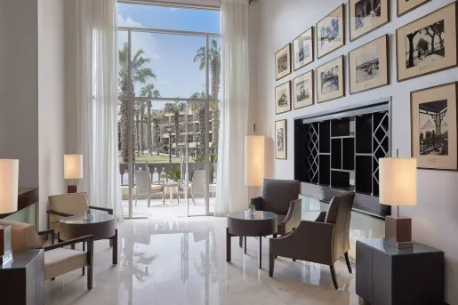 The sun-drenched lounge located inside the Marriott Mena House, Cairo features a wall covered in framed, vintage black-and-white photographs showcasing historical guests, events, and early views of the nearby Pyramids.