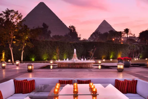 Sunset view at the outdoor lounge area at the historic Marriott Mena House, Cairo in Giza, Egypt with the Great Pyramids looming directly behind the manicured hedges.