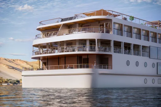 Close-up view of the stern of a luxury river cruise ship, showcasing spacious outdoor decks, private balconies, and open-air seating areas above calm river waters.