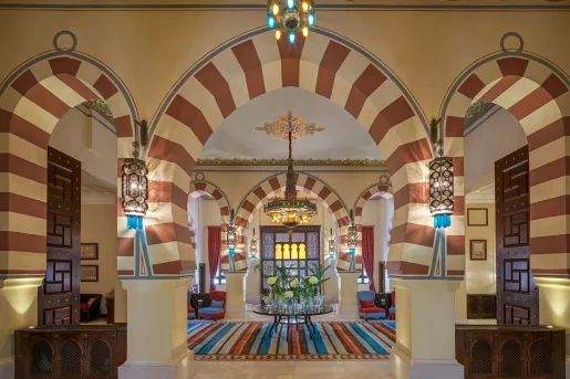 Moorish-style lobby of the Old Cataract Aswan hotel in Egypt featuring striking striped horseshoe arches, intricate hanging lanterns, and traditional geometric plasterwork.