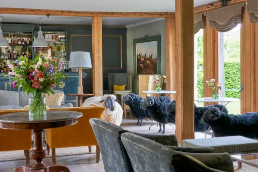 The Baa Bar inside the Thyme hotel and estate in Southrop, Cotswolds, England featuring velvet chairs and lifelike black and white sheep statues.