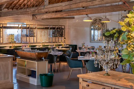 The interior of The Ox Barn restaurant at the Thyme Hotel in the Cotswold village of Southrop, Gloucestershire, United Kingdom that features industrial-style steel wine partitions, arched mirrors, and contemporary dining furnishings.