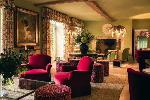  Fifi's Lounge, an elegant drawing room located inside the farmhouse at the luxury Thyme Hotel in Southrop, Cotswolds that features red velvet armchairs and gold palm-tree floor lamps.