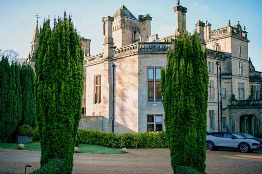 Exterior view of castle-like building with large trees and a dirt road in front