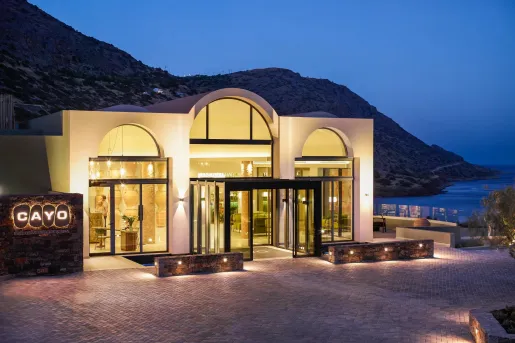 Night view of Cayo resort entrance with hills and ocean in the background.