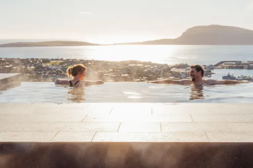 Man and woman relaxing in a large pool, with a lake in the background