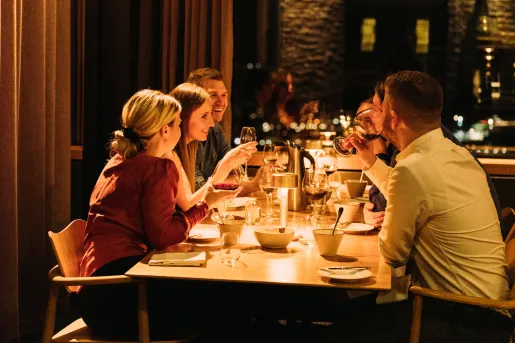 Group of people sitting at a dining table, holding glasses of wine and smiling