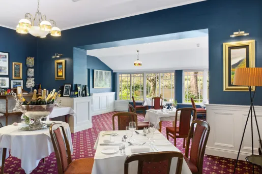 Restaurant dining hall with white tables and cushioned, red chairs in a blue room