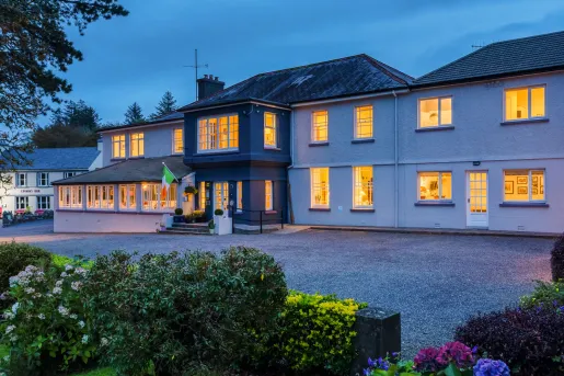 Evening, exterior view of a large white and gray building with a garden in front