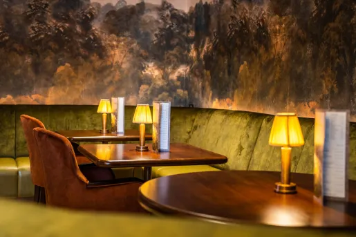 Corner of restaurant with wooden dining tables and velvet chairs