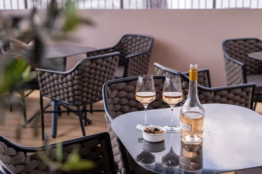 Patio with glass tables and woven chairs, with a bottle of wine and two glasses on a table