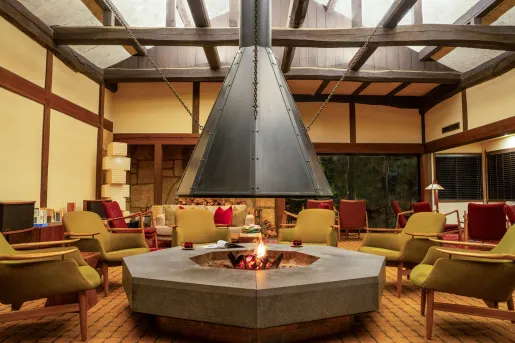 Lounge area at Ochiairo Hotel in Japan featuring a large central hearth with an open fire, wood-beam ceilings, comfortable seating arranged in a circle, and warm ambient lighting inspired by traditional Japanese design.