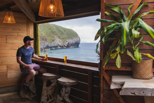 Man sitting on a stool, holding a beer and looking out towards the ocean