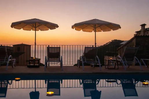 Outdoor pool with umbrellas and reclining chairs, with the sunset in the distance